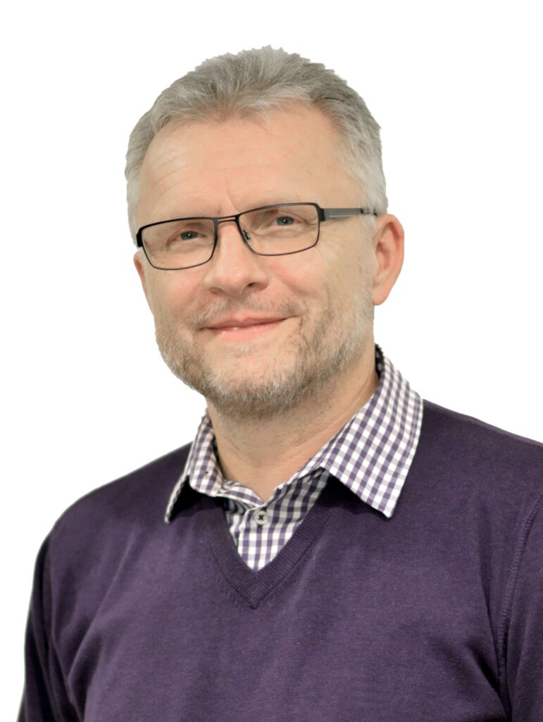 Sympathischer Mann mit Brille und Bart in lila Pullover - vertrauensvoller Ansprechpartner bei YANA Bestattung.